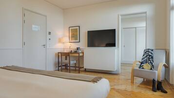 Una habitación de hotel con una cama, un escritorio con una silla, un televisor y un perchero con botas.