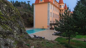 Un grand bâtiment doté d’une piscine, d’un patio avec des chaises longues et surplombant un paysage montagneux.