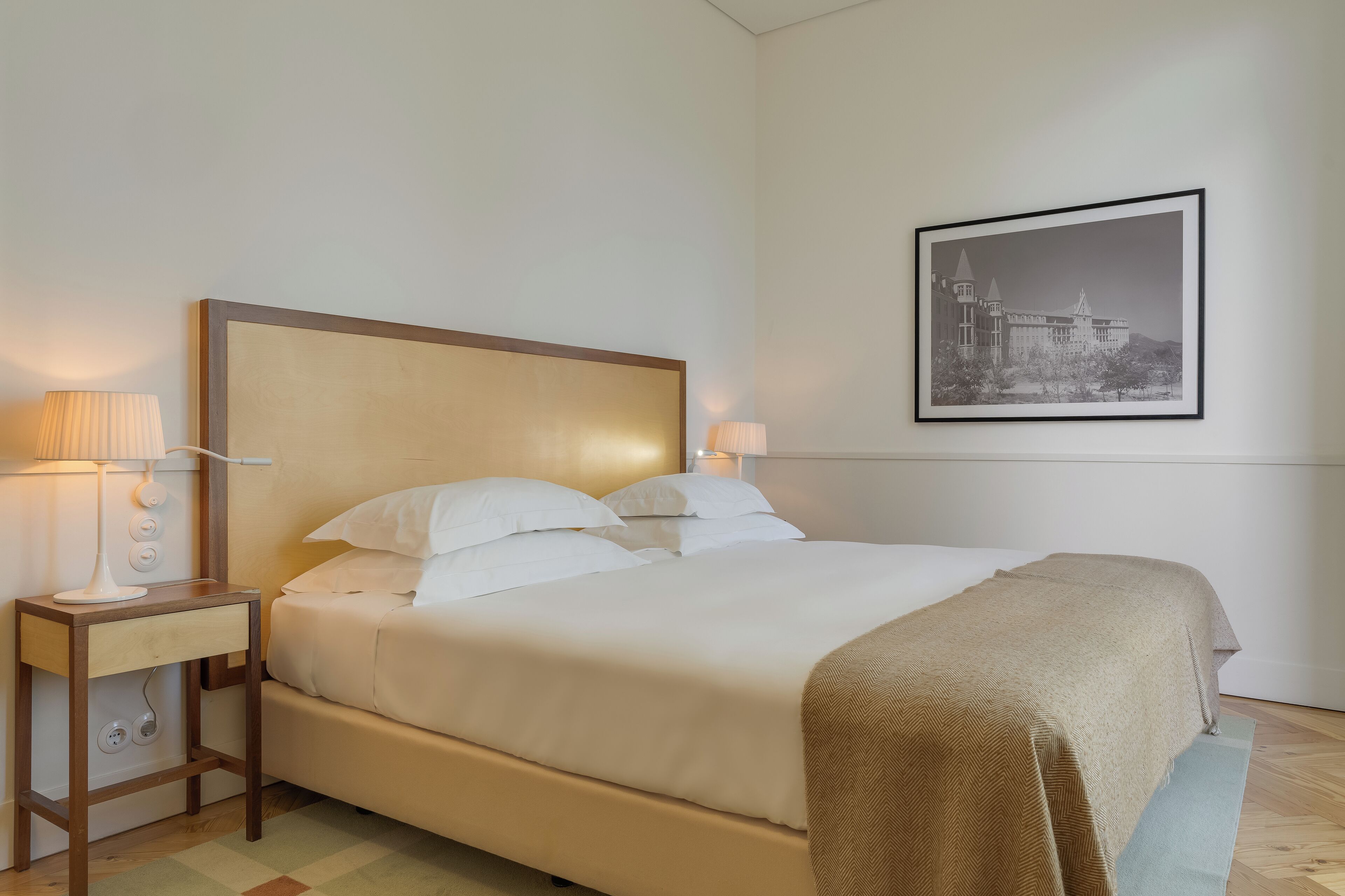 A neatly made bed with a headboard, two bedside tables with lamps, and a framed picture on the wall.