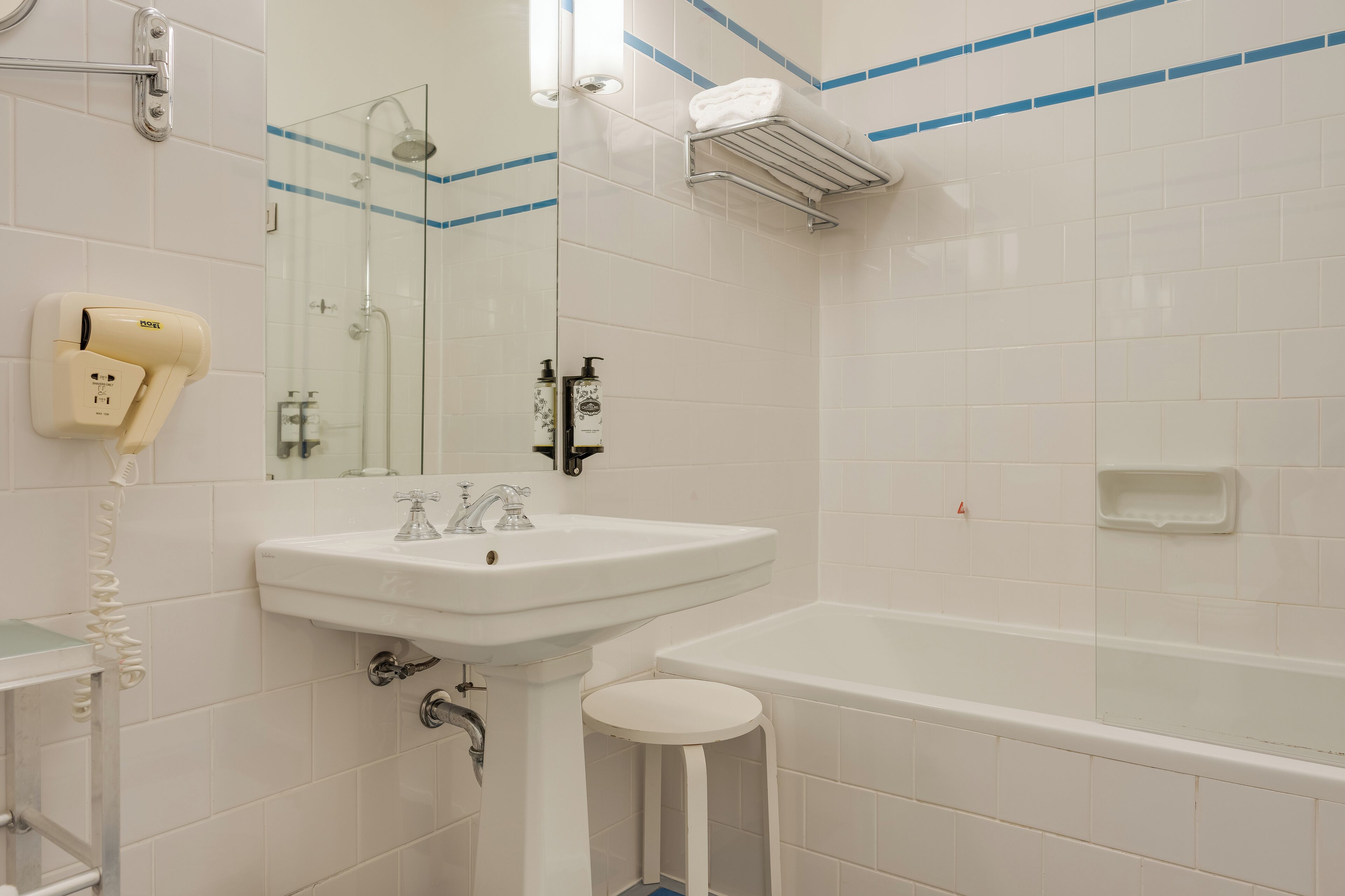 A bathroom with a white sink, a mirror, a handheld hair dryer, a shower, and a bathtub.