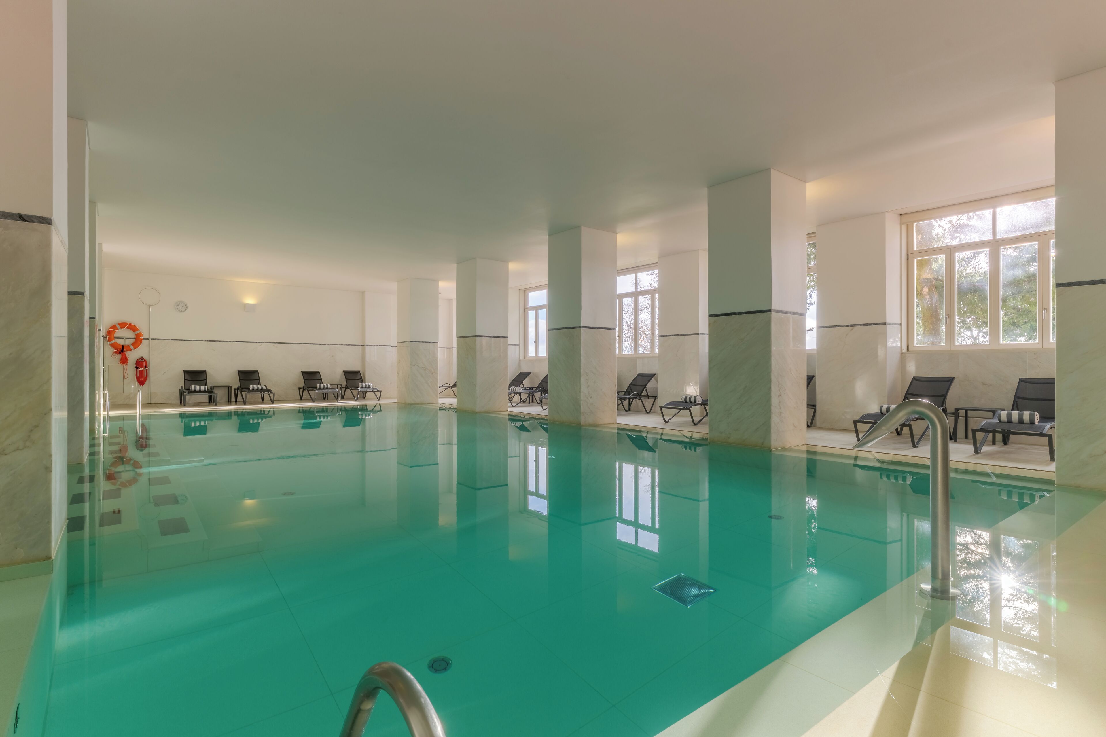 Piscina interior con agua cristalina, rodeada de sillones de descanso y un aro de baloncesto.
