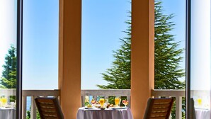 Un balcon avec deux chaises en bois et une table dressée pour le repas, offrant une vue sur un ciel dégagé et une végétation luxuriante.