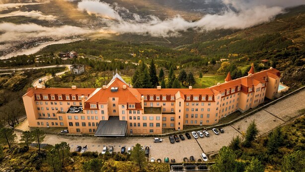 Un grand hôtel à plusieurs étages, doté d’une cour intérieure et entouré d’un paysage montagneux.
