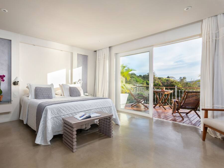 A modern bedroom with a large bed, a bedside table, a window, and a balcony with outdoor furniture.