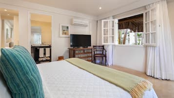 A bedroom with a large bed, a TV, a wooden dresser, a chair, and a window with curtains.