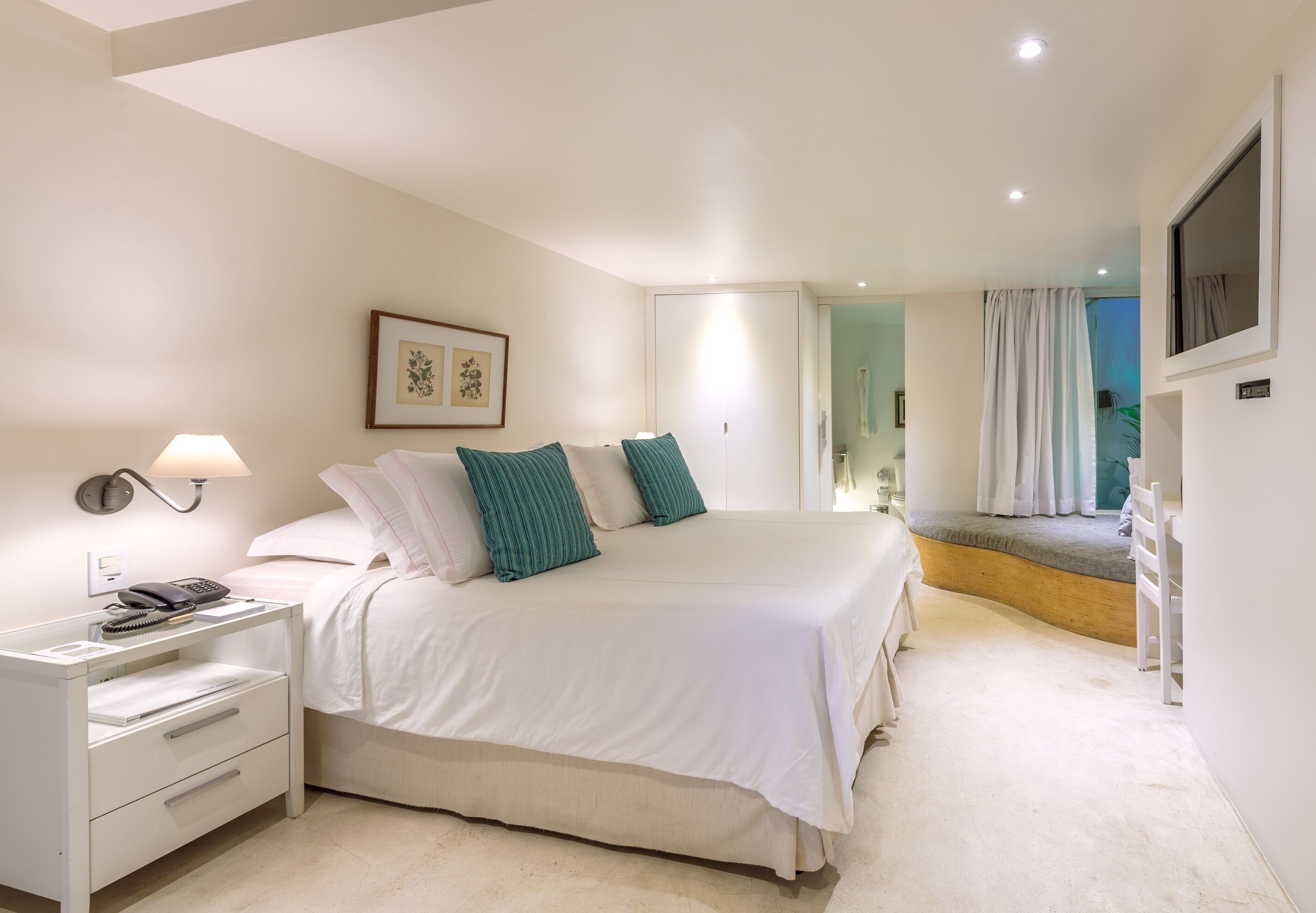 A bedroom with a bed, bedside table, lamp, and a view of a balcony.