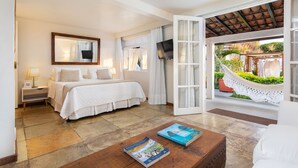 A hotel room with a bed, a TV, a large window, and a view of a garden. - Abracadabra Boutique Hotel (Búzios)