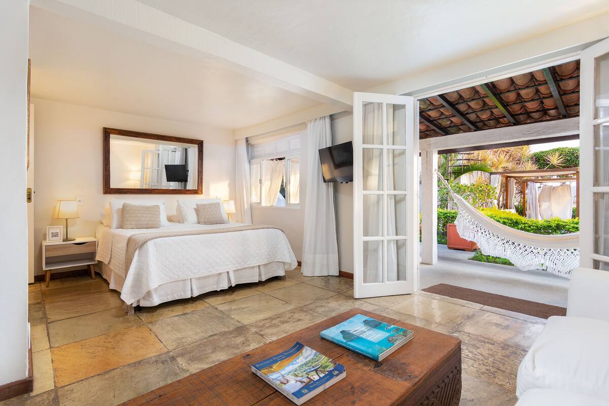 Habitación de hotel con cama, televisor, ventana grande y vistas a un jardín.
