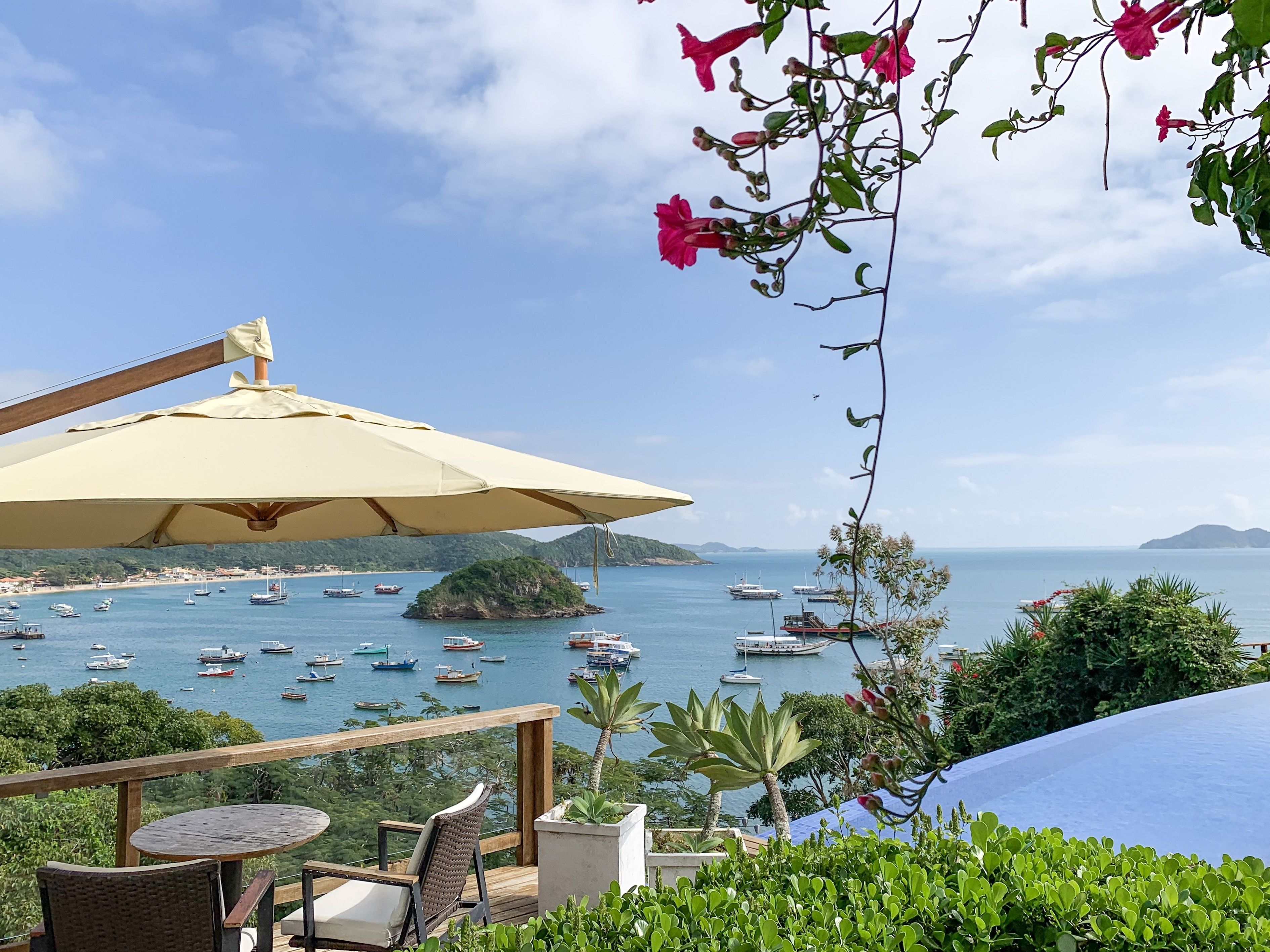 Una terraza con mesa y sillas, con vistas a una zona costera con barcos y vegetación.