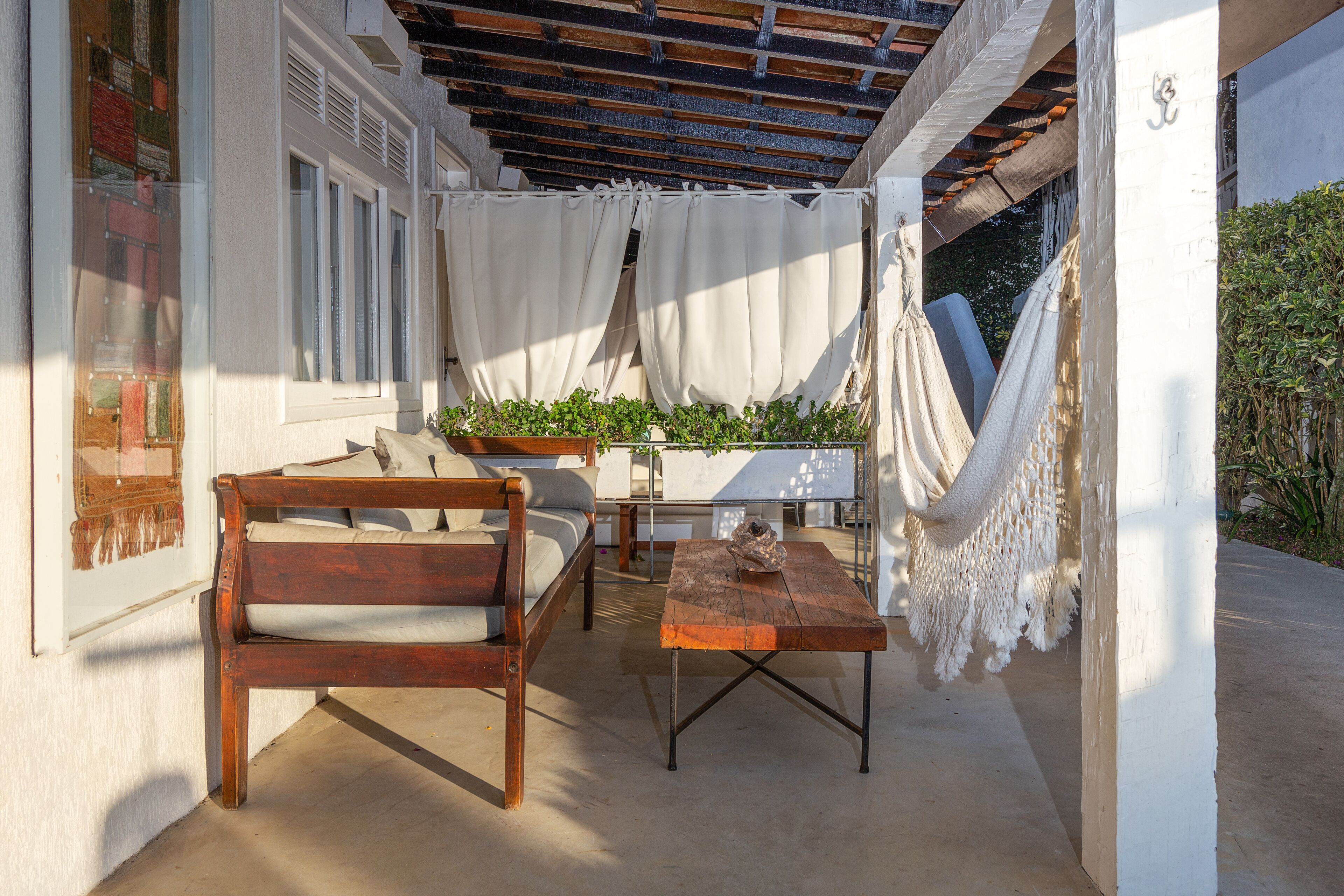 An outdoor patio with a wooden bench, a table, and a hammock.