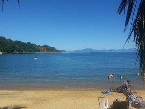 A beach with clear blue water, a sandy shore, and a few people swimming and relaxing. - Pousada dos Golfinhos (Angra dos Reis)