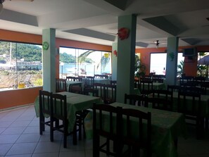 A restaurant with multiple tables and chairs, large windows with a view of the sea and greenery, and a tiled floor. - Pousada dos Golfinhos (Angra dos Reis)