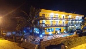 Un hotel de varios pisos con zona de piscina, mobiliario exterior y ubicación frente a la playa.