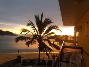 A beach view with a palm tree, chairs, and a building in the foreground. - Pousada dos Golfinhos (Angra dos Reis)