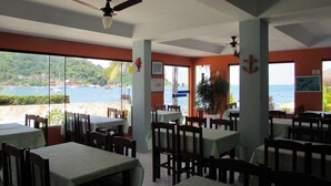 Un restaurante con mesas y sillas, un ventilador de techo y vista al mar.
