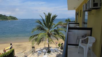 Uma varanda com vista para uma praia, uma palmeira e algumas cadeiras de praia.