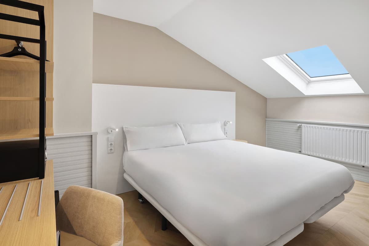 A bedroom with a skylight, a bed, a wooden desk, and a chair.