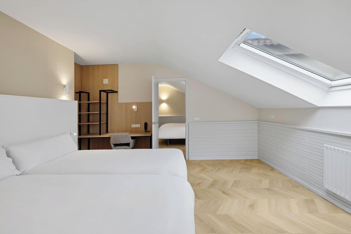 A bedroom with a sloped ceiling, a skylight, a bed, a desk, and a chair.
