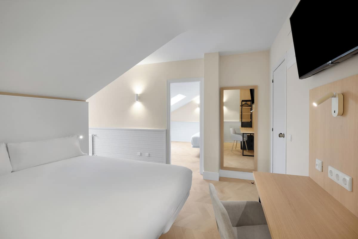 A modern bedroom with a large bed, a wooden desk, and a TV mounted on the wall.