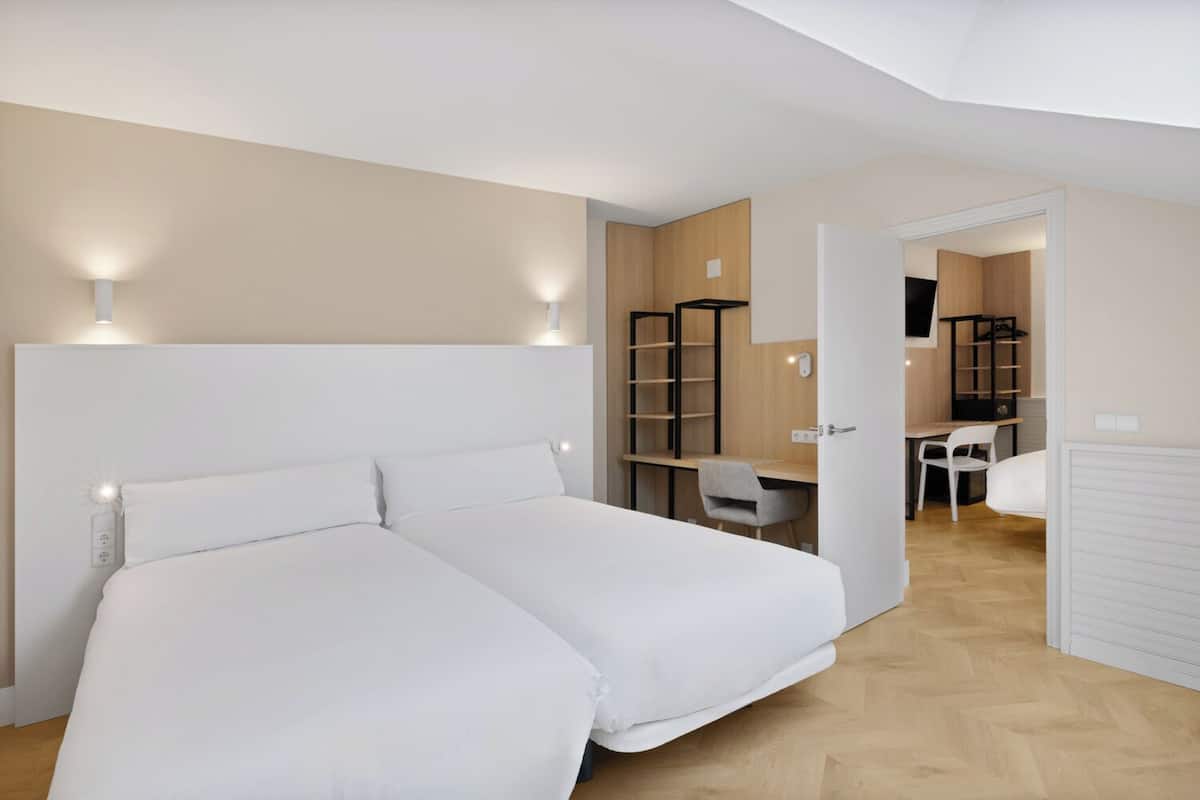 A bedroom with two beds, a desk, and a chair.
