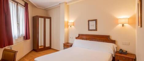 Una habitación de hotel con una cama individual, mesitas de noche, un armario y dos lámparas de pared.