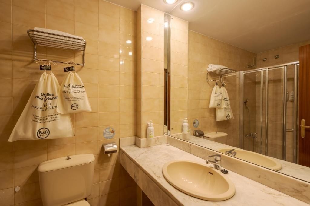 A bathroom with a toilet, sink, mirror, and shower.