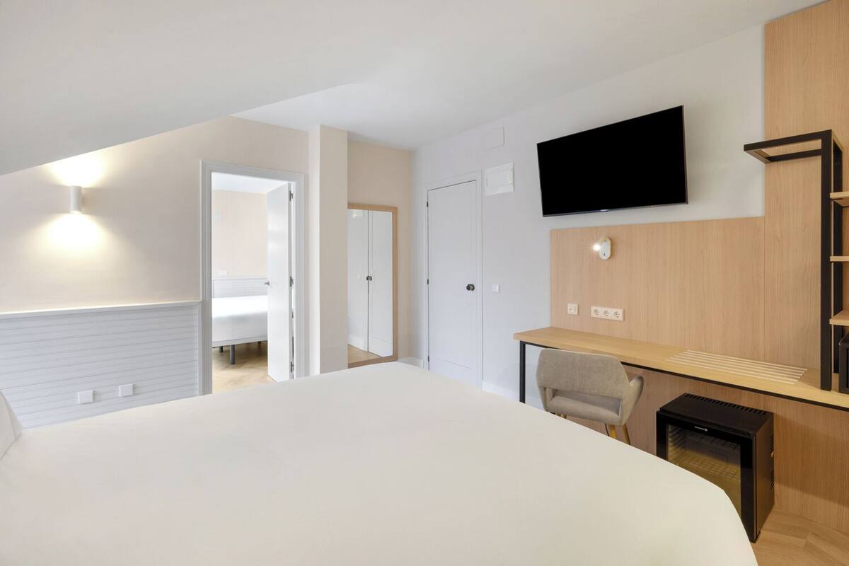 A modern hotel room with a large bed, a desk with a chair, a television mounted on the wall, and a wardrobe.