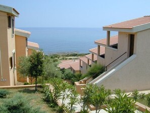 Un hôtel situé sur la côte, doté de nombreux balcons, de toits en tuiles de terre cuite et offrant une vue sur la mer.