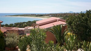 A coastal view with buildings, a beach, and mountains in the distance. - Il Borgo di Porto Corallo (Villaputzu)