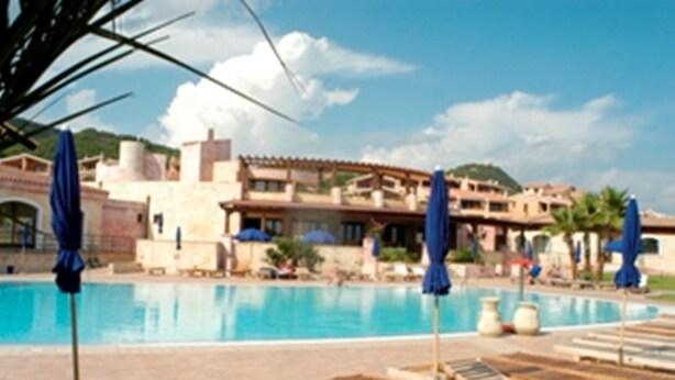 A swimming pool with lounge chairs and umbrellas, surrounded by buildings with a Mediterranean architectural style. - Il Borgo di Porto Corallo (Villaputzu)