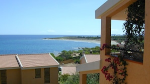 A view of a coastal area with a building featuring a balcony with a view of the sea and a garden with flowering plants. - Il Borgo di Porto Corallo (Villaputzu)