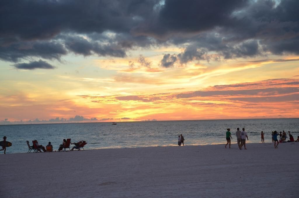 A beach with people relaxing and walking along the shore during sunset.