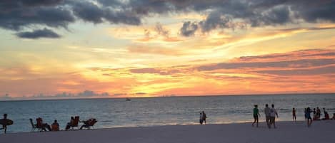 A beach with people relaxing and walking along the shore during sunset.