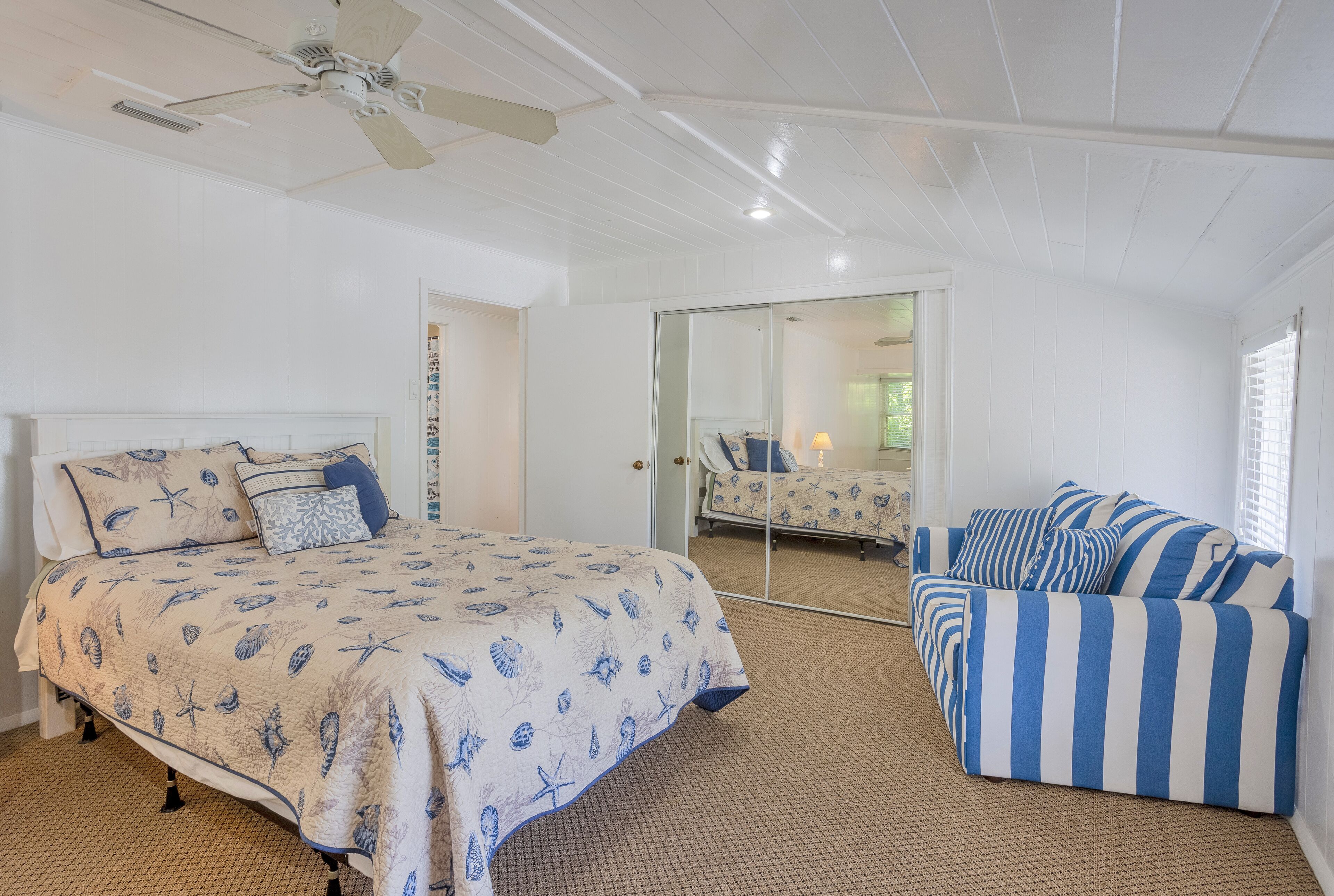 A bedroom with a bed, a sofa, a ceiling fan, and a large mirror.