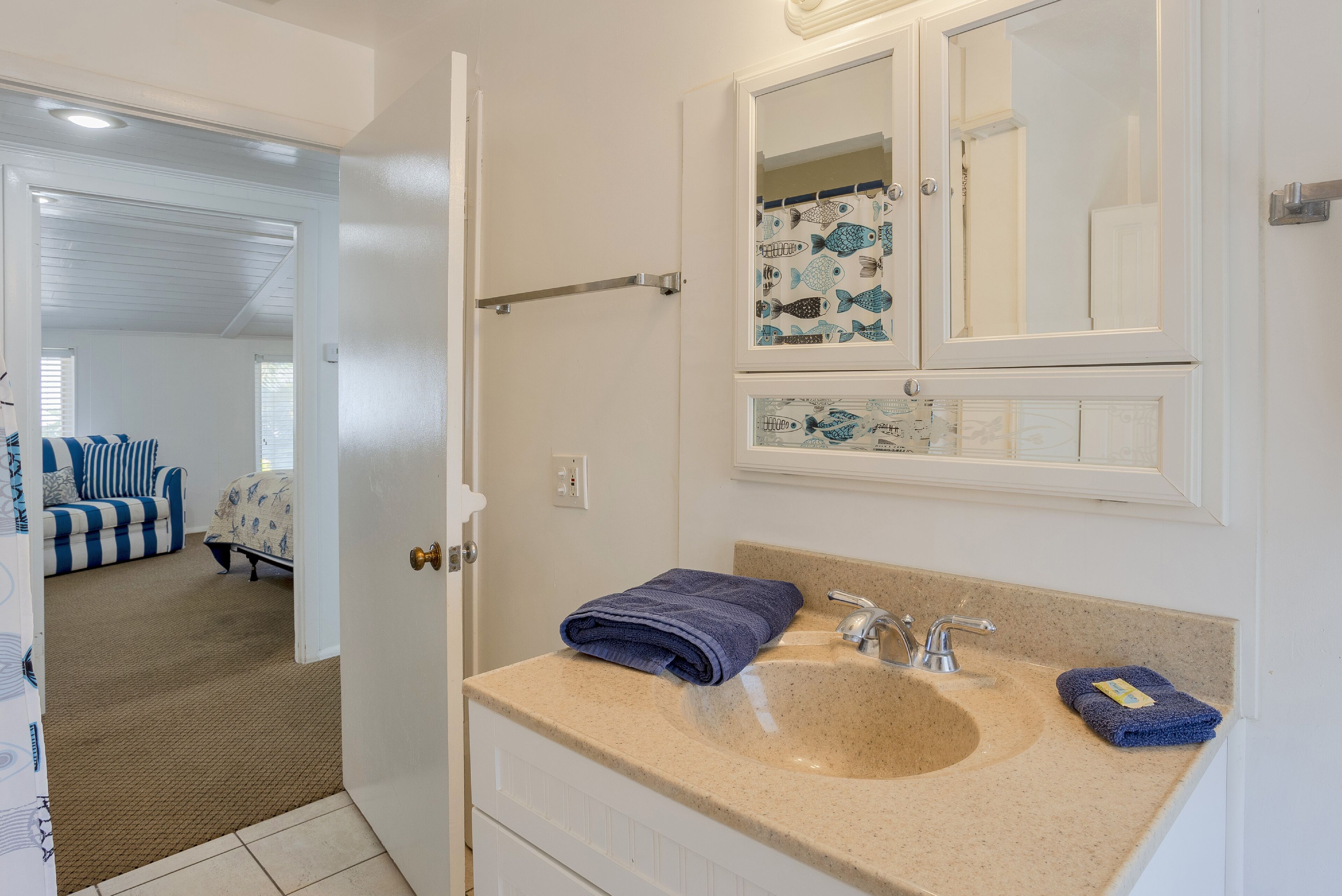 Un baño con un lavabo color beige, un espejo con motivos de peces y un perchero para toallas.