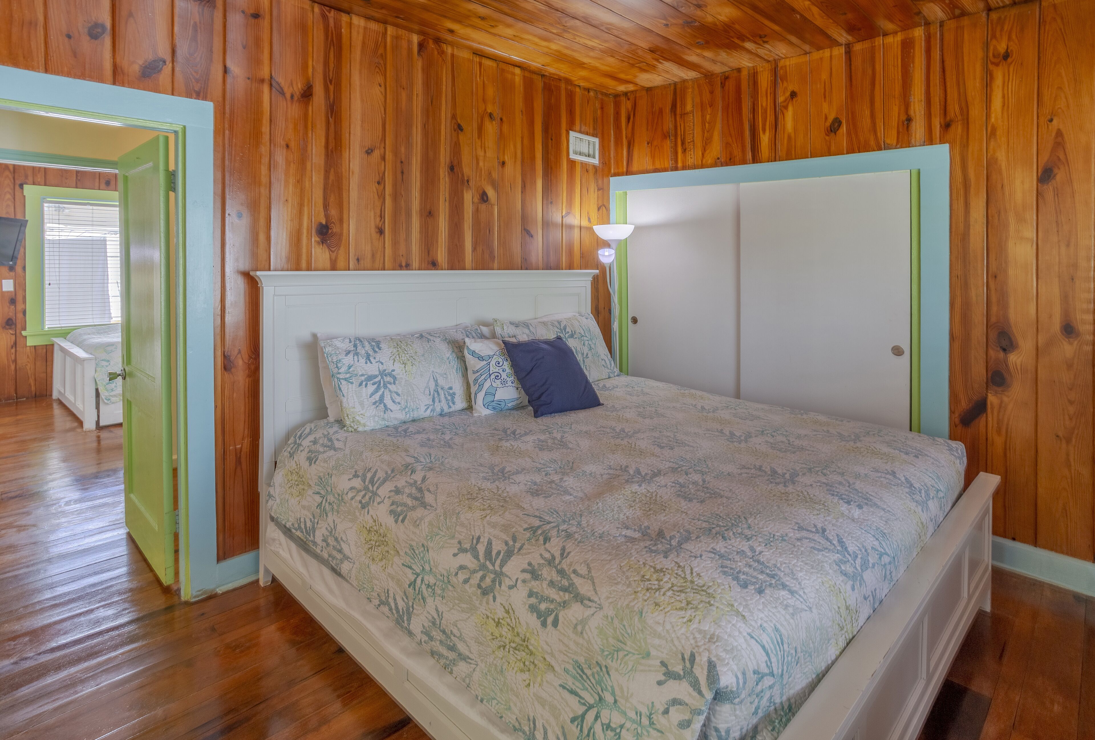 Una camera da letto con pareti in legno, un letto con lenzuola a motivi floreali, un comodino e una porta con cornice verde.