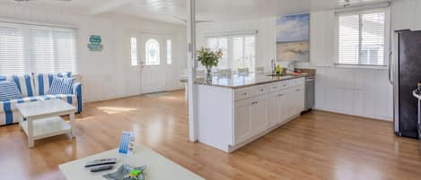 A spacious living area with a white sofa, a coffee table, and a kitchen area with white cabinets and a granite countertop.
