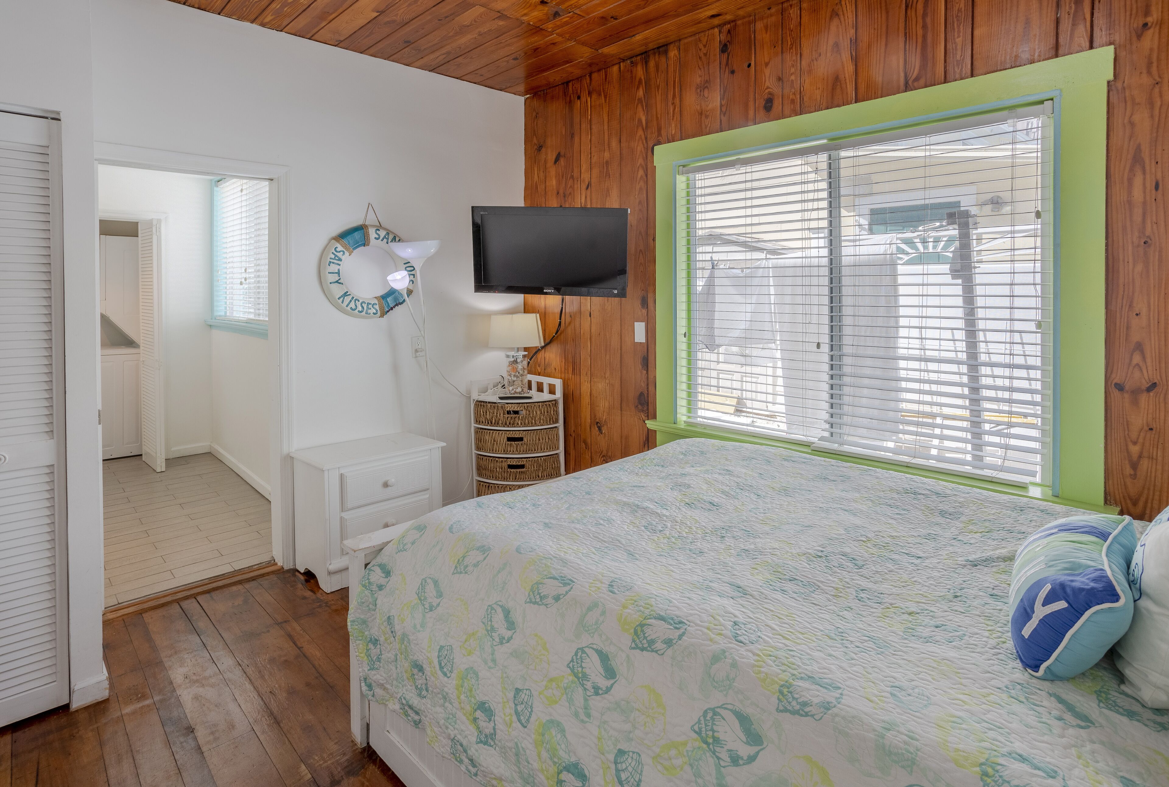 A bedroom with a bed, a television, a window with blinds, a lamp, and a wall decoration.