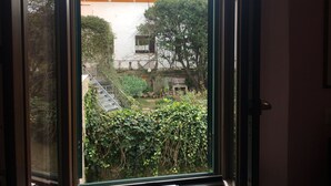 A view through a window of a building with a staircase leading to a balcony, surrounded by greenery and a fence. - La Maison dei Miracoli (Pisa)