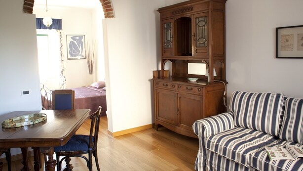A room with a wooden dining table, a striped sofa, a wooden cabinet, and a chandelier. - La Maison dei Miracoli (Pisa)