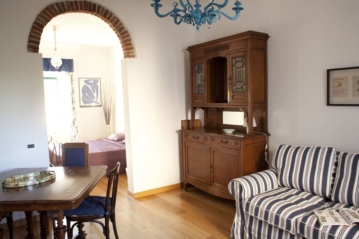 A room with a wooden dining table, a striped sofa, a wooden cabinet, and a chandelier.