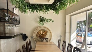 A restaurant with a long wooden table, chairs, a fan, a decorative wall, and a view of the street outside. - Hotel Maria Eugenia Tuxtla Gutierrez (Tuxtla Gutierrez)