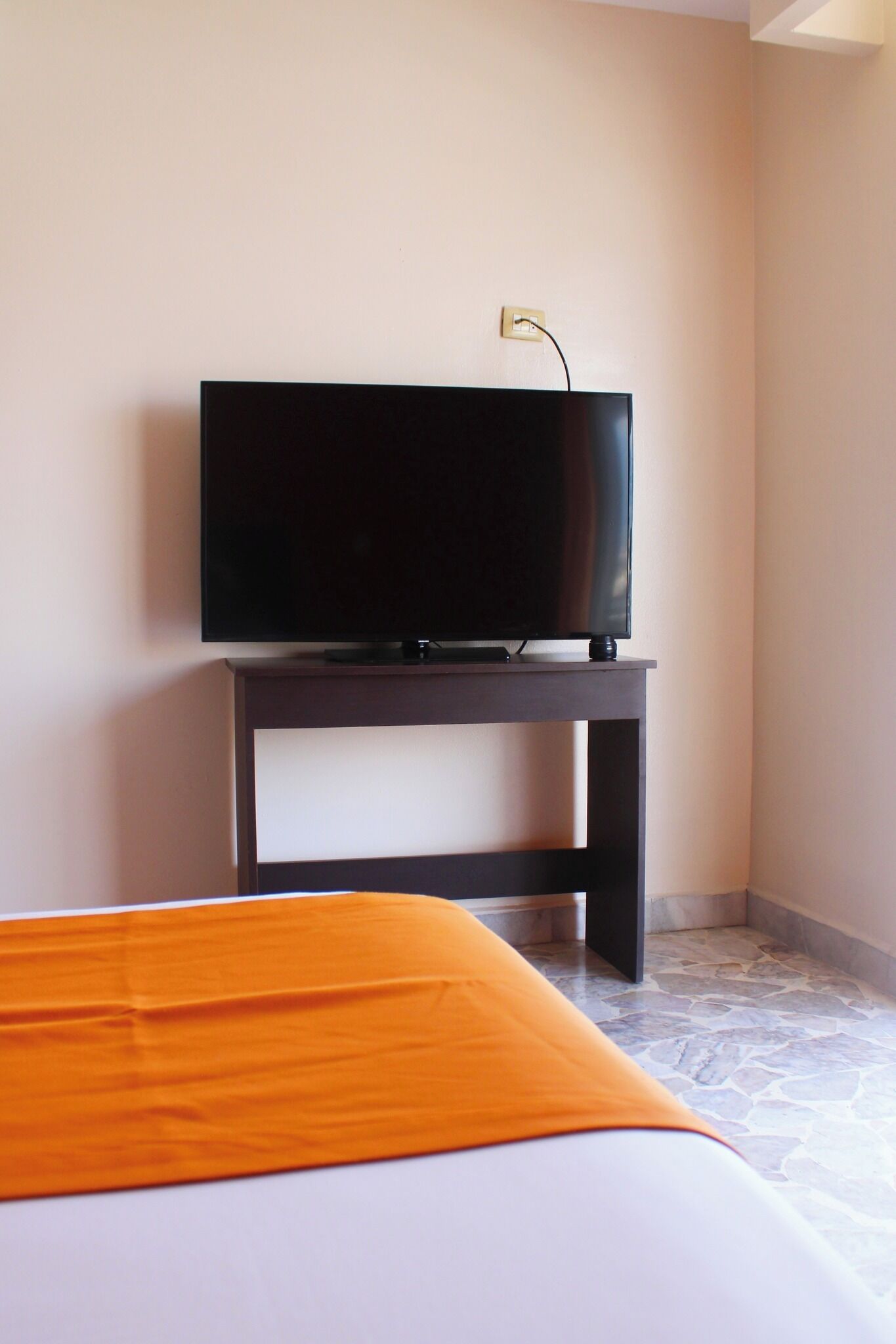 A room with a bed, a television on a stand, and a wall socket.