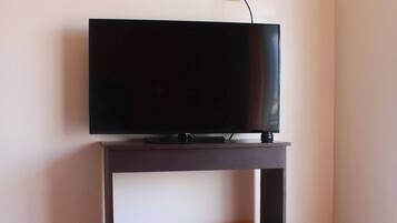 A room with a bed, a television on a stand, and a wall socket.