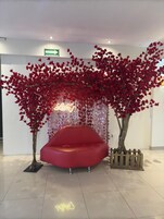 A red sofa in a lobby with artificial red trees and a neon sign.