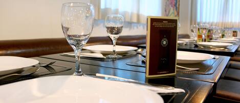 A dining table set with plates, cutlery, and wine glasses, with a menu stand and a painting in the background.