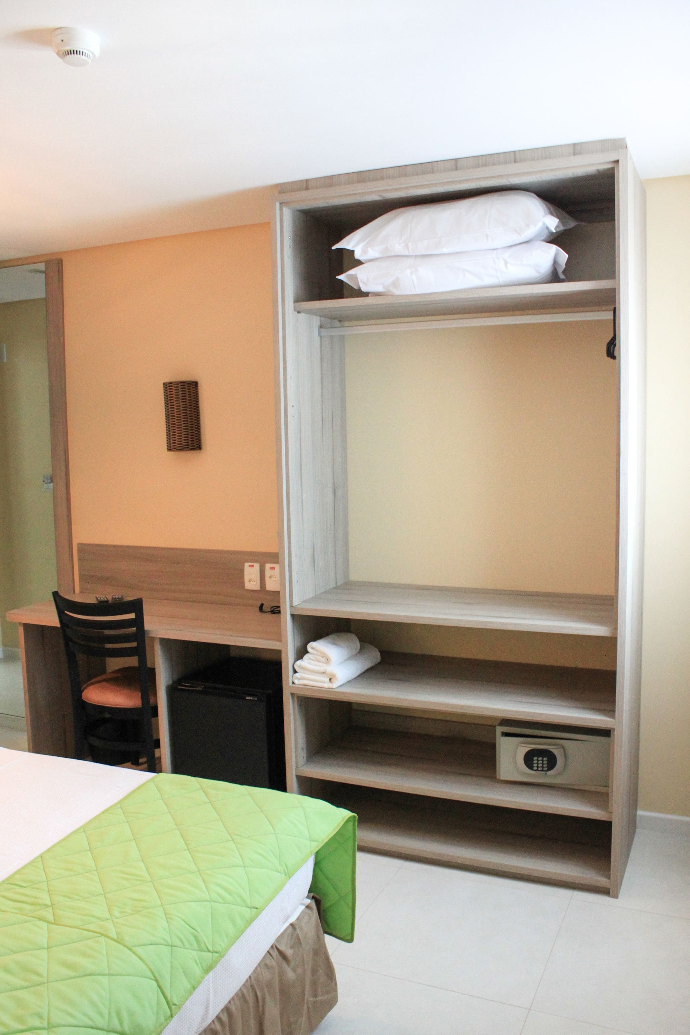 Une chambre d’hôtel équipée d’un lit, d’un bureau, d’une chaise, d’une armoire et d’une petite poubelle.