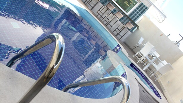 A swimming pool with a tiled floor and metal handrails. - Hotel Anahi (Jaboatão dos Guararapes)