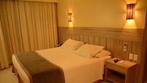 A hotel room with a large bed, wooden headboard, two bedside lamps, a nightstand, and a curtain. - Hotel Anahi (Jaboatão dos Guararapes)