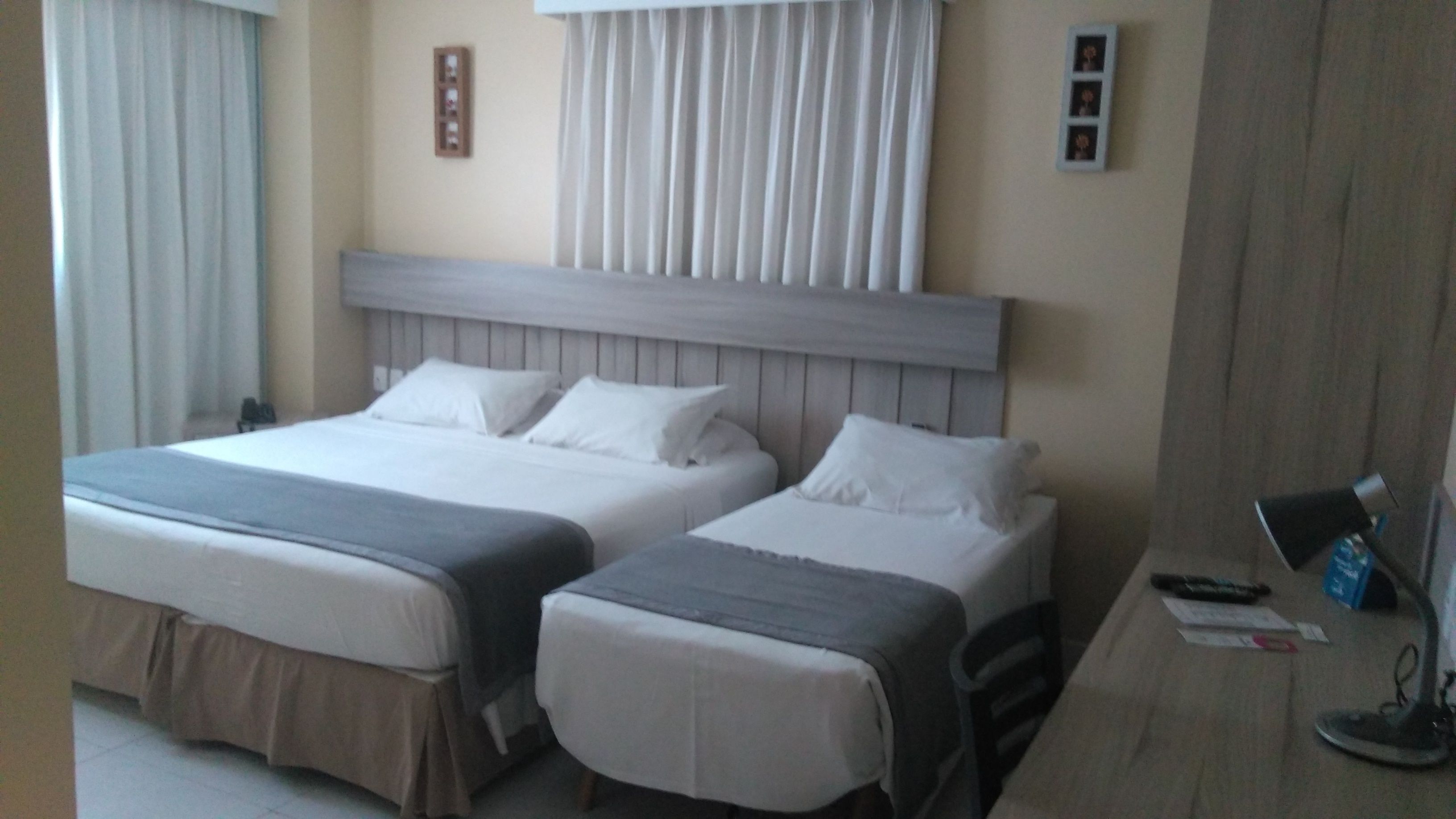 Habitación de hotel con dos camas, cabecero de madera, escritorio con silla y ventana con cortinas.